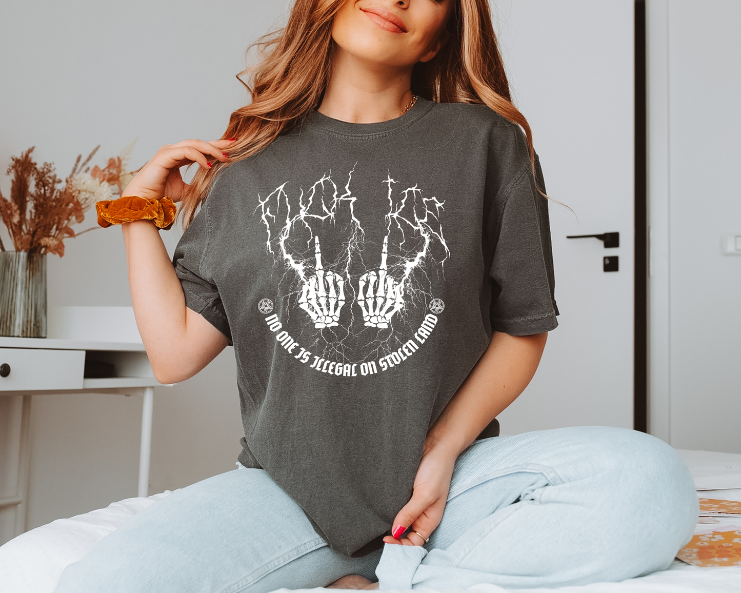 Woman wearing a dark gray t-shirt with a graphic design, sitting on a bed.